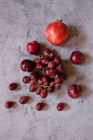 still life raw plums, pomegranate and grapes in a grey stone backgroundの写真素材