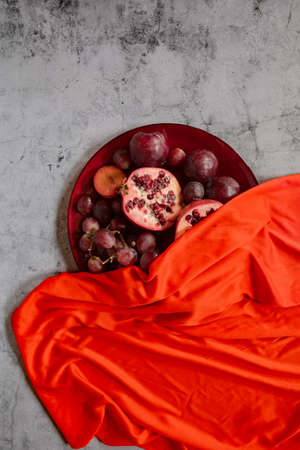raw plums, pomegranate and grapes covered in red in a grey stone backgroundの写真素材