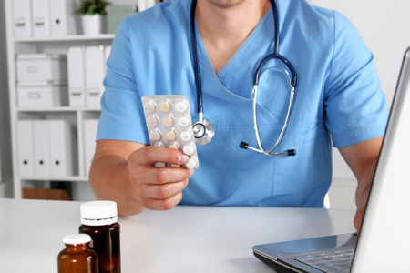 Male doctor sitting at the table and holding bottle with pills.の写真素材