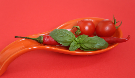Fresh cherry tomatoes and chili on red plate.の写真素材