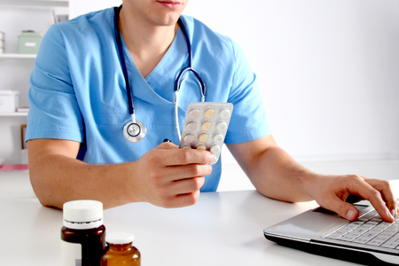 Male doctor sitting at the table and holding bottle with pills.の写真素材