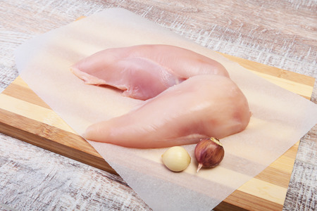 Raw chicken breast fillets and garlic ready for cooking on wooden boardの写真素材