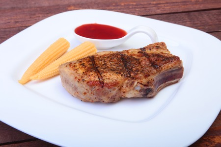 grilled pork chop with Cranberry sauce and Mini Corn cob preserved on plate on wooden boardの写真素材