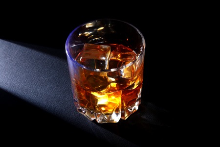 Glass of whiskey or bourbon with ice on black stone table.の写真素材