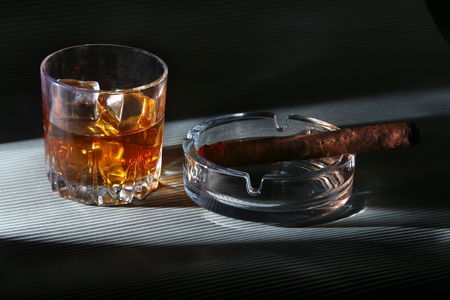 Glass of whiskey or bourbon with ice and cigar on black stone table. Selective focus.の写真素材