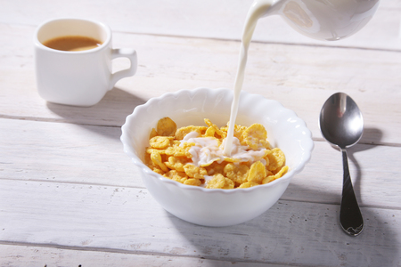 Milk pouring into a bowl of delicious corn flake cereals and cap with espresso coffee. Morning breakfast.の写真素材