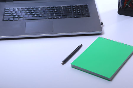 Modern white office desk table with laptop, smartphone and other supplies. Blank notebook page for...