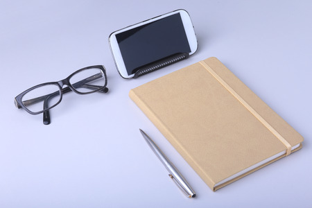 Business concept. Top view of kraft spiral notebook, glasses, smartphone and black pen isolated on background for mockup.の写真素材