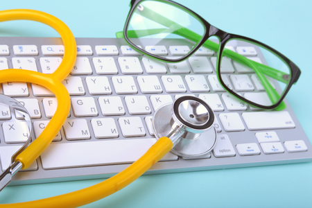 Closeup of a yellow stethoscope lying on notebook keyboard and green glasses. selective focus.の写真素材