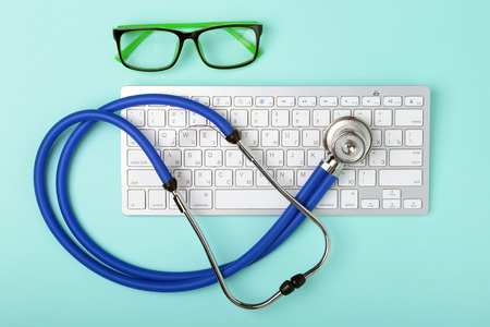 Closeup of a blue stethoscope lying on notebook keyboard and green glasses. selective focus.の写真素材