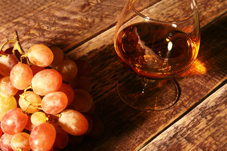 Cognac or Brandy in a glass and fresh grapes, still life in rustic style, vintage wooden background, selective focus.の写真素材