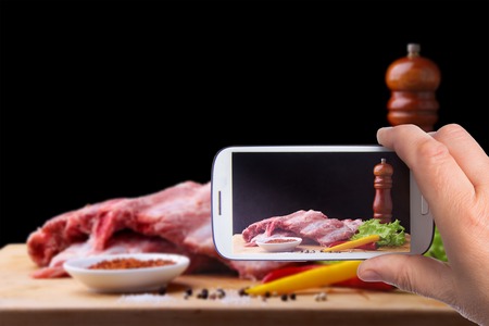 Hands of man with smartphone taking photo Raw Ribs on a rustic cutting board with salt, pepper and grinder for spicesの写真素材