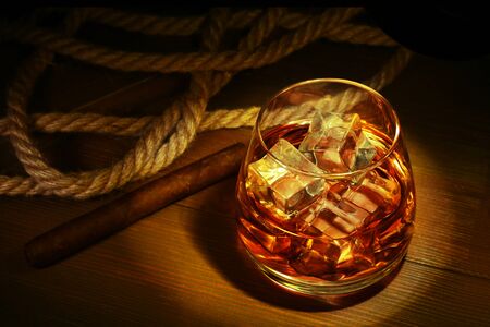 Glass with whiskey, ice cubes and smoking pipe on wooden background.の写真素材