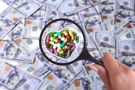 concept of Health insurance. Assortment pills in magnifier against the background of Many dollar banknotesの写真素材
