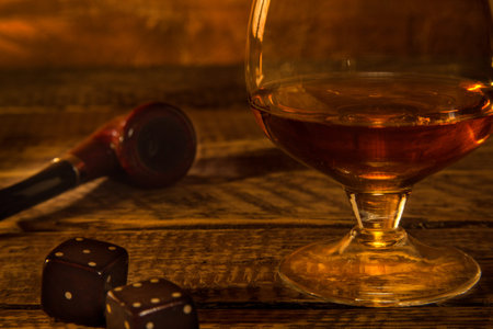 Glass with cognac or whiskey and smoking pipe on a wooden table.
