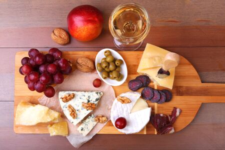 Assortment of cheese with fruits, grapes, nuts, glass with wine and cheese knife on a wooden serving trayの写真素材
