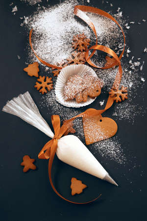 Christmas gingerbread cookies with confectionery mastic snowflakes and pastry bag with icing on black background, view from above. Holiday food, homemade baking, Christmas and New Year traditions.の写真素材