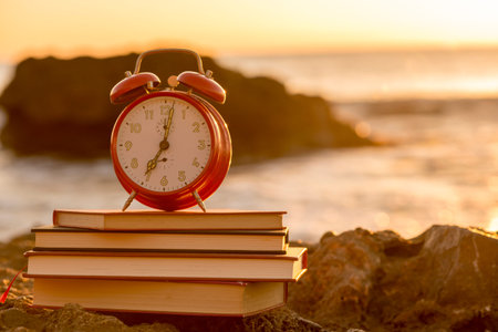 An alarm clock on top of some books by the sea at dawnの写真素材