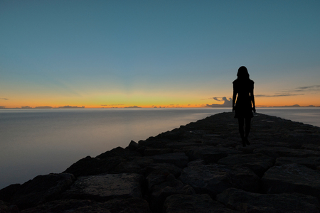 Silhouette of a woman walking by the sea at nightの写真素材