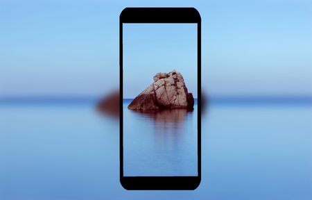 A mobile phone with the blue sea in the backgroundの写真素材