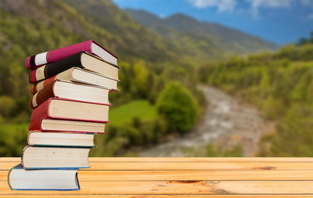 Books on a table with the mountain and river in the backgroundの写真素材