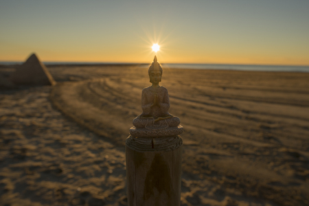 Figure of a buddha meditating by the sea in a beautiful sunriseの写真素材
