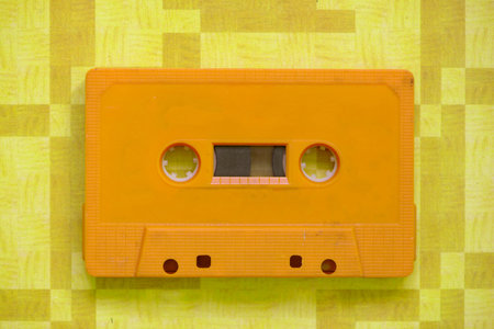 A retro cassette tape of a yellow color with orange background