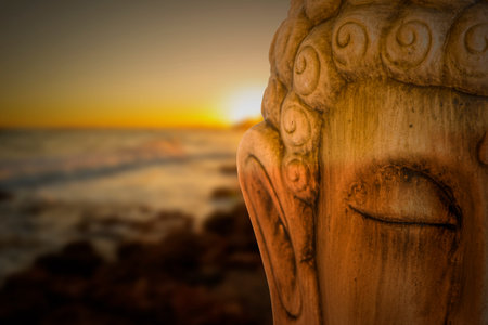 Buddha figure meditating with a sunrise on the beach, Spain