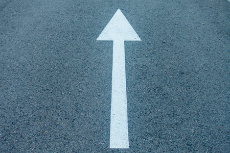 A white arrow going straight painted on the asphalt