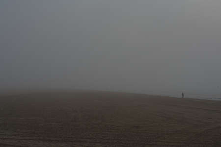 a lonely person walks on the beach on a foggy dayの写真素材