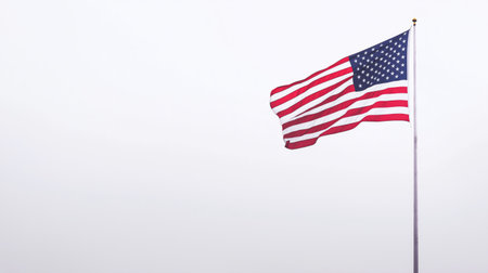 A vibrant American flag flutters on a tall pole, showcasing its red, white, and blue colors. The scene captures a bright day with no clouds in sight, emphasizing patriotism.の素材