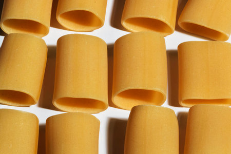 Three lines of pasta paccheri on a white background, the pasta shape is highlighted by the light direction, top view, golden yellow colorの写真素材