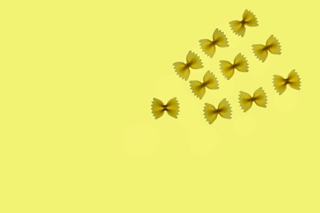 Raw pasta farfalle arranged on a yellow background, top view, funny compositionの写真素材