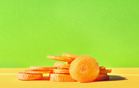 Slices of carrot on a colored background, studio shot, green and orange colors in perfect harmony, vibrant colors, front viewの写真素材