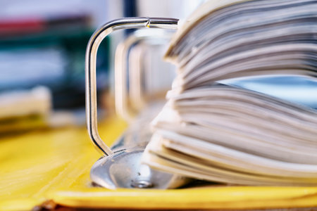 Open yellow binder close up , stack of white papers and bright metal rings , in the background...