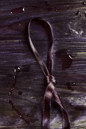 Dark purple and knotted  ribbon on wooden background ,  several bright  water drops on the backgroundの写真素材