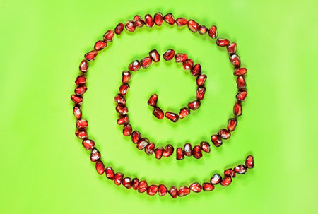 Beautiful spiral shape with red pomegranate seeds on green background