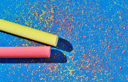Yellow and red thick stick of chalk on blue background, small pieces of yellow and red chalk scattered on the backgroundの写真素材