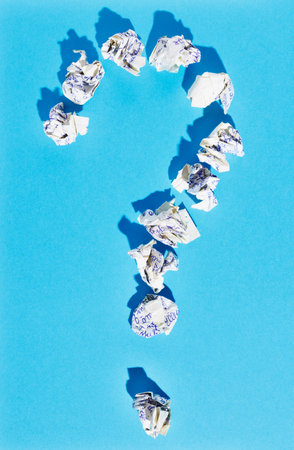 Symbol of question made by crumpled paper on blue background, white hand written paper