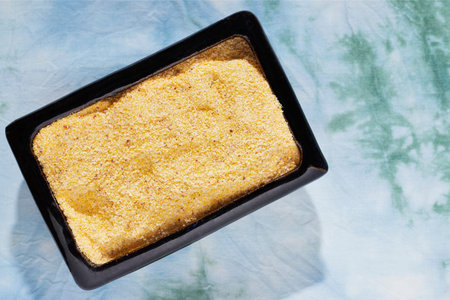 Heap of uncooked polenta in blue bowl, yellow grains of cornmeal