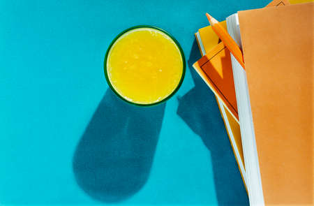 Fresh orange juice in blue glass on blue background, books with orange covers and one orange pencil,の写真素材