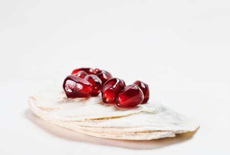 Bright red seeds of pomegranate on white seashellの写真素材