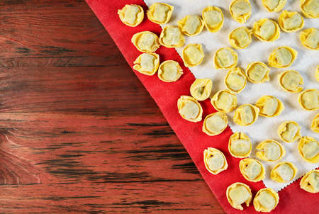 Italian tortellini on white cloth, uncooked stuffed pasta on red wooden tableの写真素材