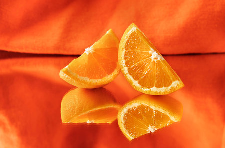 Slices of orange fruit on mirror on orange background, mirror reflection,