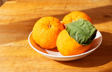 Oranges in white plate on wooden table , fresh fruit with green leaves , healthy eatingの写真素材