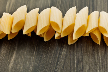 Italian pasta penne on dark table, tubular pieces of furrowed pasta with ends cut at an angle made with durum wheat semolina and waterの写真素材
