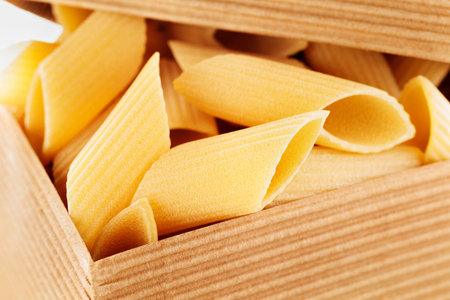 Italian pasta penne in box, tubular pieces of furrowed pasta with ends cut at an angle made with...