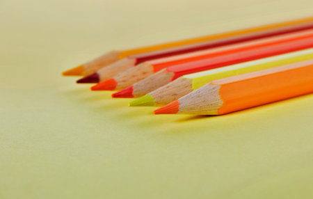 Pointed red, yellow and orange wooden pencils on yellow background, place of work or leisure timeの写真素材