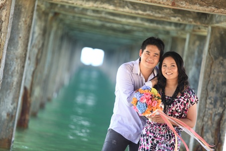 couple standing outdoors smiling under pier on the beachの写真素材