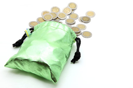 coins spilling out from green money bag or purse isolated on whiteの写真素材